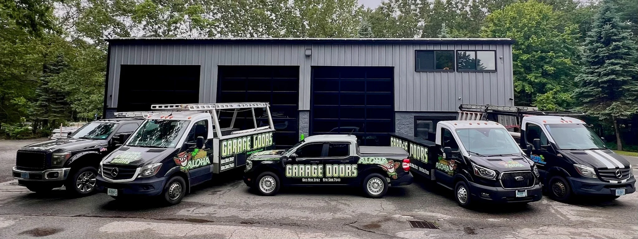 A fleet of branded service trucks parked outside a commercial warehouse building for an Overhead Door Company